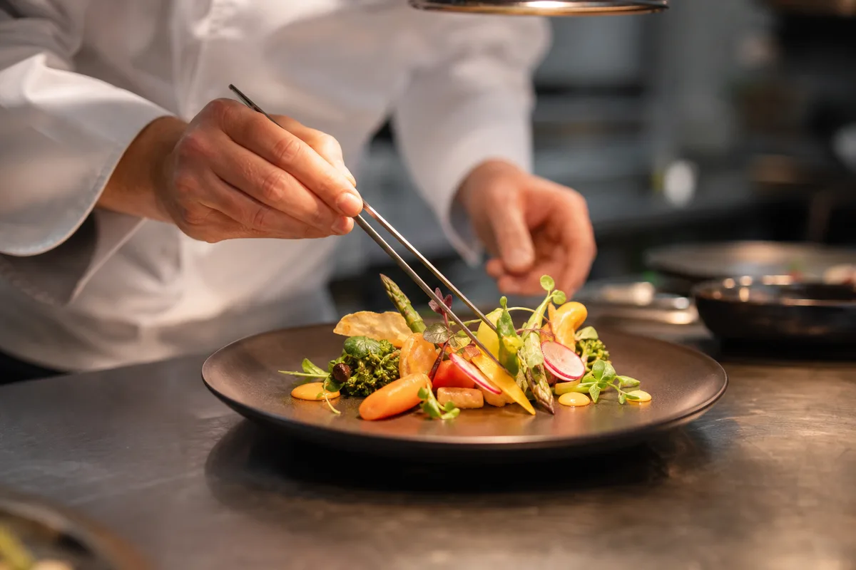 Chef dressant un plat végétarien gastronomique au moment du service dans une cuisine professionnelle