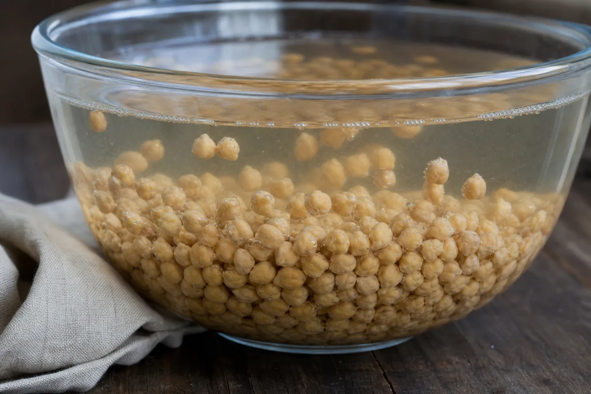 Pois chiches secs en cours de trempage dans un grand saladier en verre rempli d’eau claire