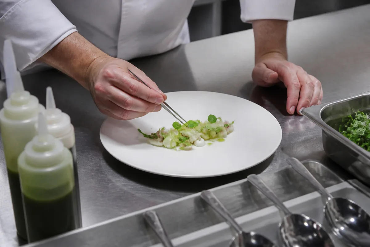 Chef posant un élément à la pince sur une assiette blanche en cuisine professionnelle